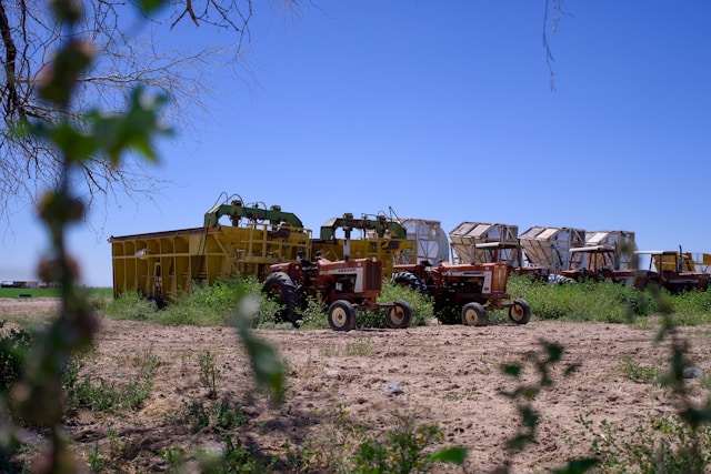 Cour de ferme avec deux tracteurs rouges rustiques devant une grange ouverte remplie de paille.