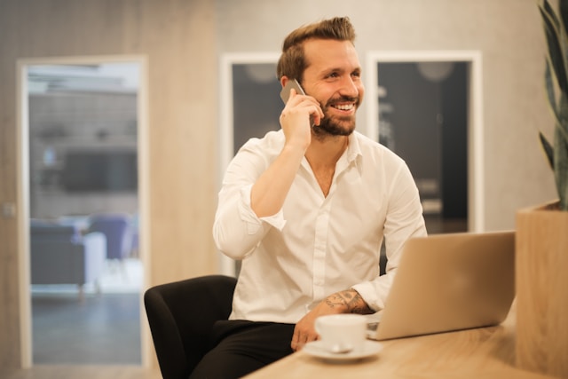 Un professionnel souriant au téléphone devant son ordinateur portable dans un bureau moderne, représentant un échange fluide avec un client grâce au suivi de facturation de CashNow